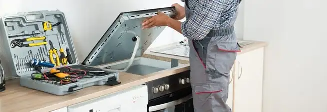 Cooktop repair technician lifting a built-in stovetop for service in Aurora, CO