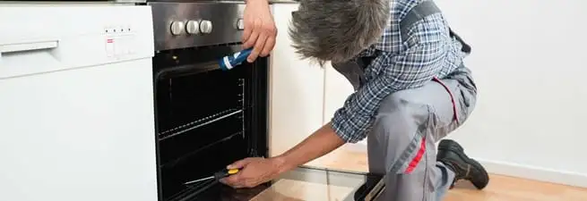 Oven repair technician inspecting and servicing an electric oven in Aurora, CO