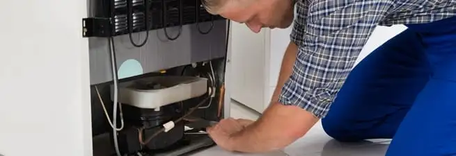 Refrigerator repair technician servicing the compressor and condenser area in Aurora, CO
