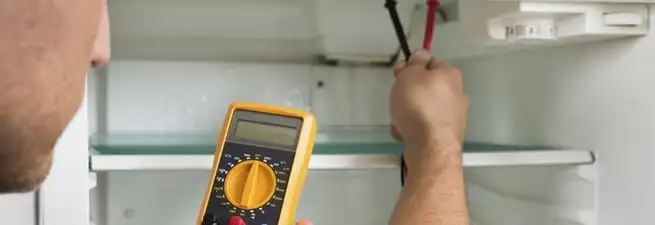 Refrigerator repair technician testing electrical components with a multimeter in Aurora, CO