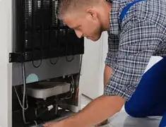 Refrigerator repair technician servicing the compressor and condenser area in Aurora, CO